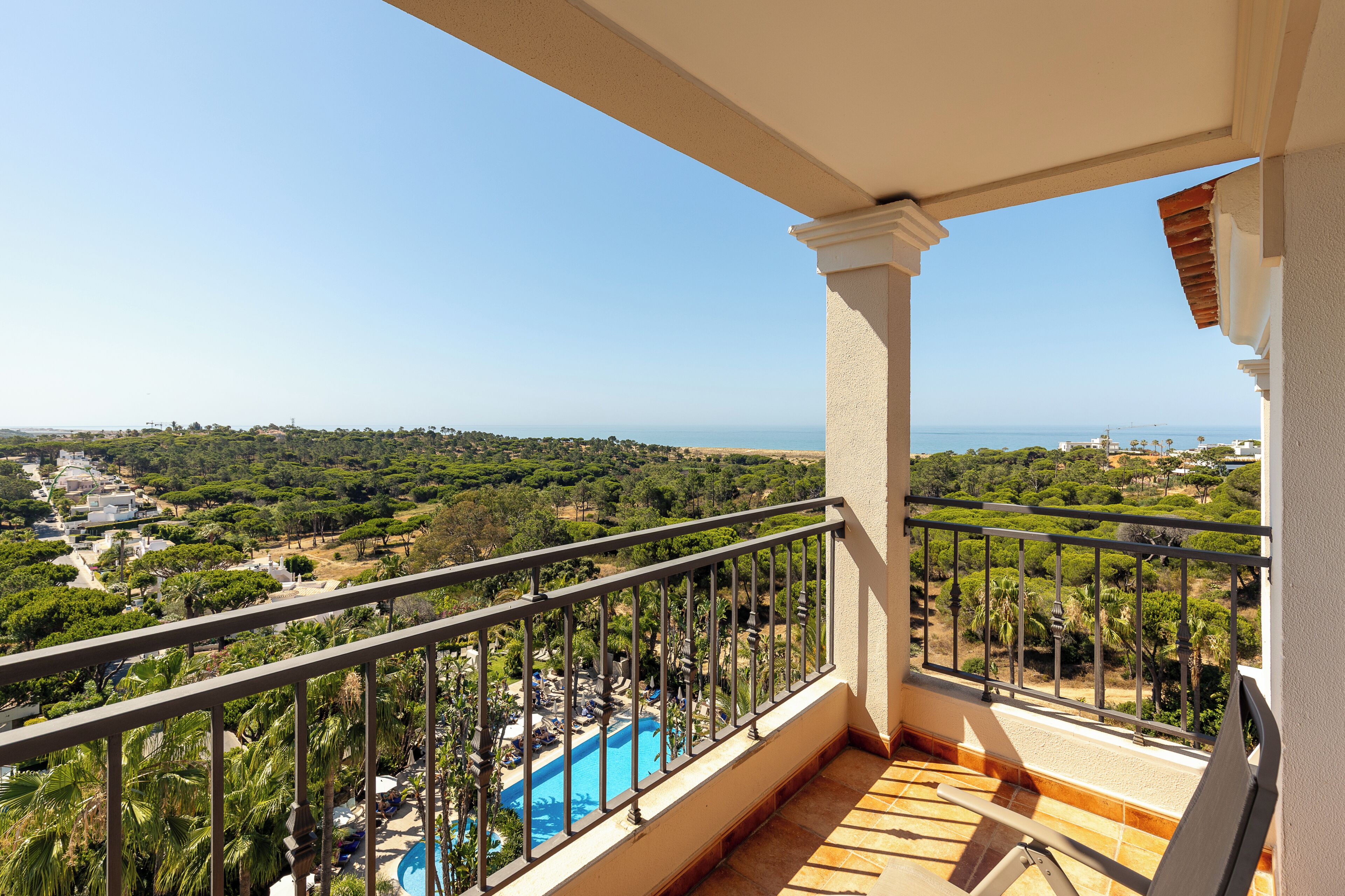 A balcony with a pool, overlooking a coastal landscape with greenery and buildings.