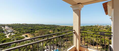 A balcony with a pool, overlooking a coastal landscape with greenery and buildings.