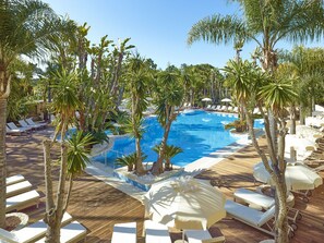 A pool area with lounge chairs and umbrellas, surrounded by palm trees.