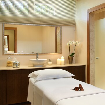 A hotel bathroom with a large mirror, a sink, candles, and a bed with a white bedspread.
