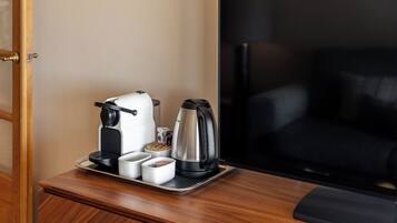 A hotel room with a wooden nightstand holding a coffee maker, a kettle, and a tray with cups and a box of tissues.