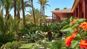 A tropical garden with palm trees and a building with a red roof. - Ria Park Hotel & Spa (Loulé)