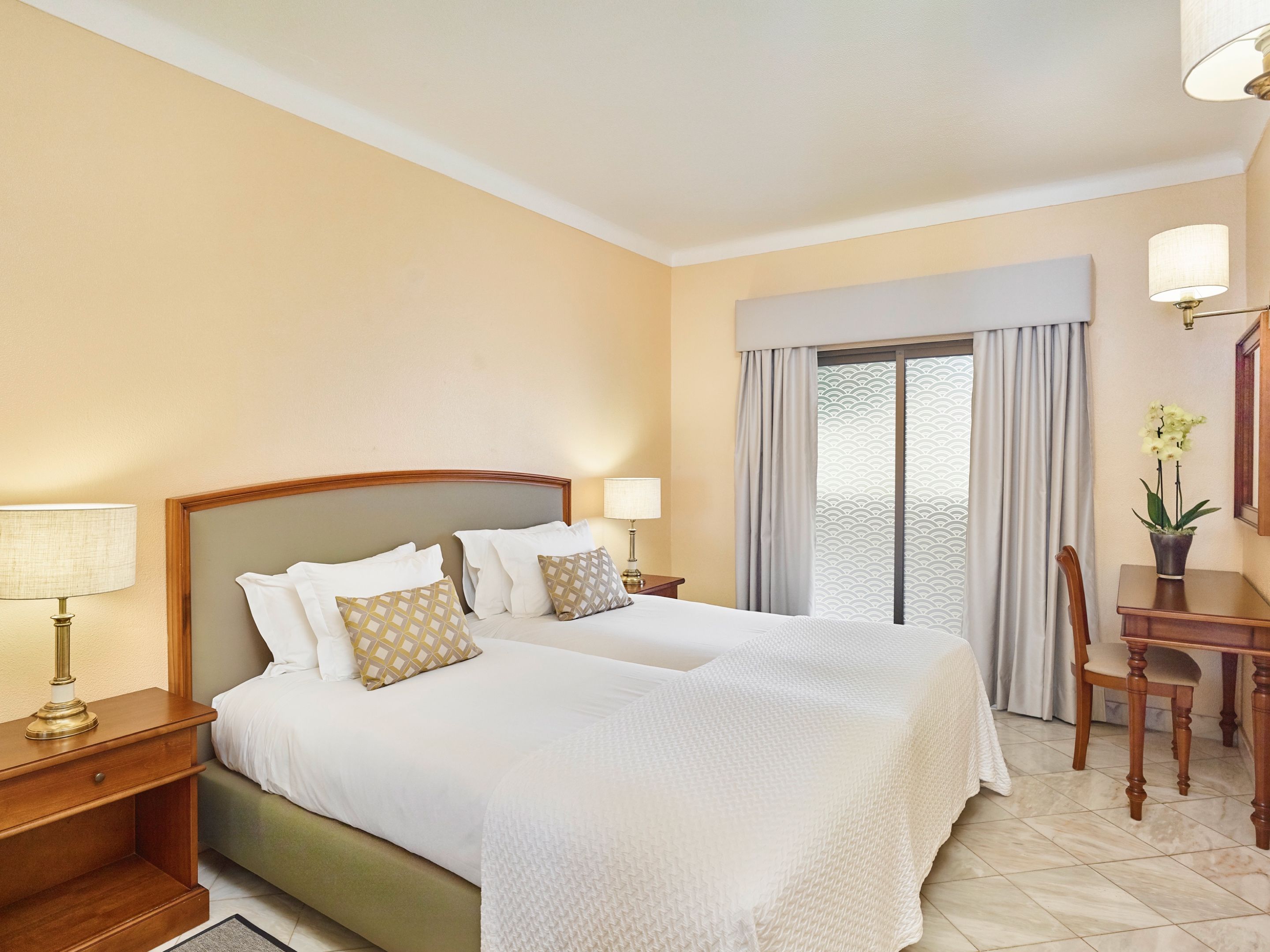 Habitación de hotel con una cama grande, dos mesitas de noche, un escritorio con silla y una ventana con cortinas.