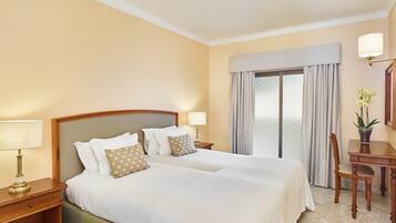 Habitación de hotel con una cama grande, dos mesitas de noche, un escritorio con silla y una ventana con cortinas.