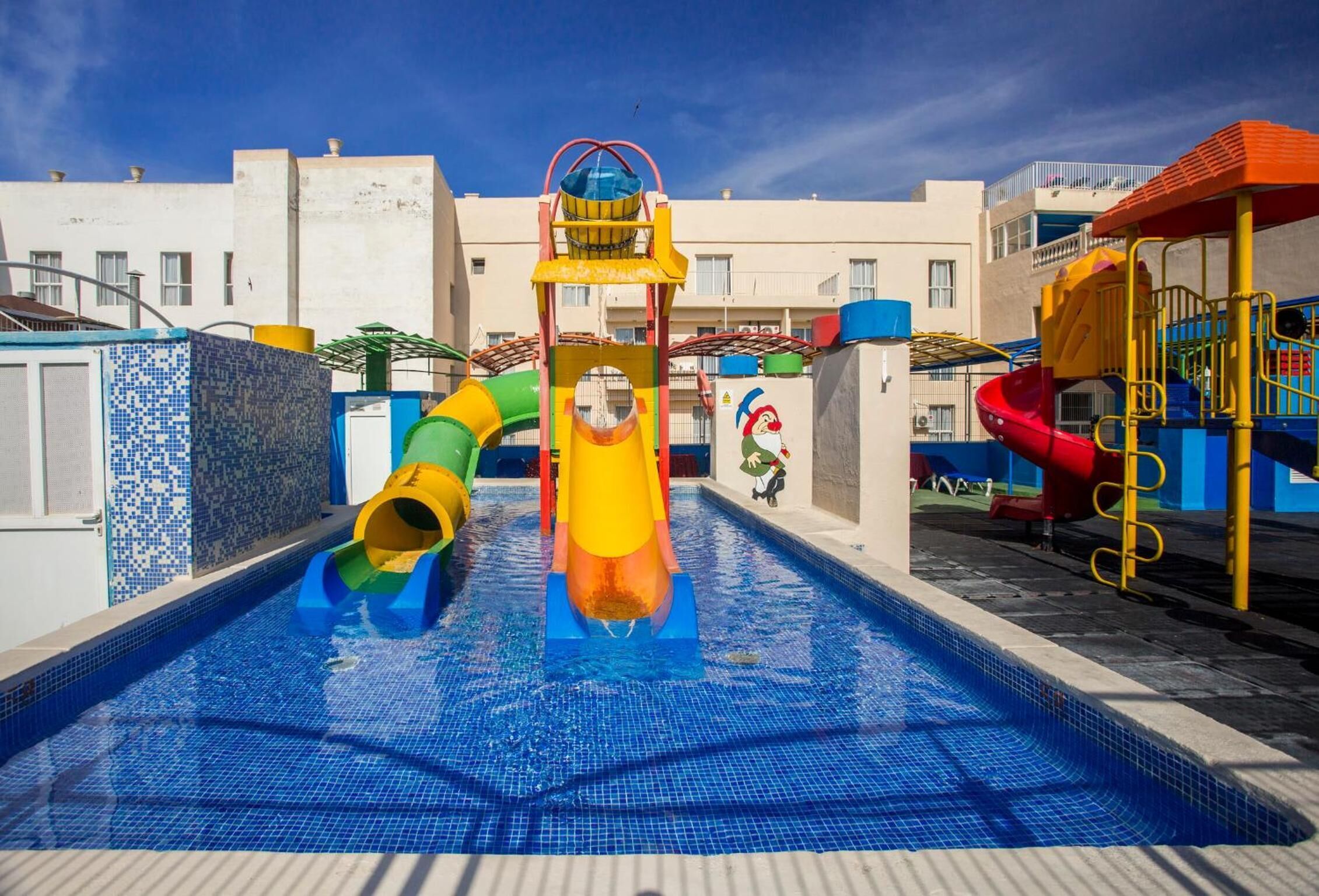 A swimming pool with colorful slides and a children's play area.