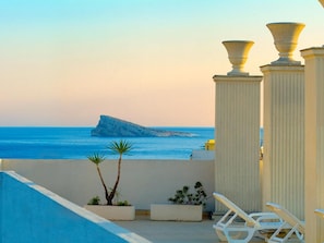 Una terraza con vistas al mar, que incluye una formación rocosa, plantas en macetas y sillones blancos para relajarse.