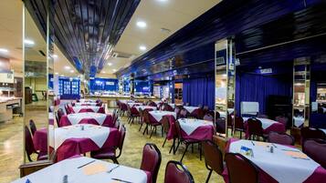 Un salón de banquetes con mesas dispuestas para comer, sillas y una zona de escenario.