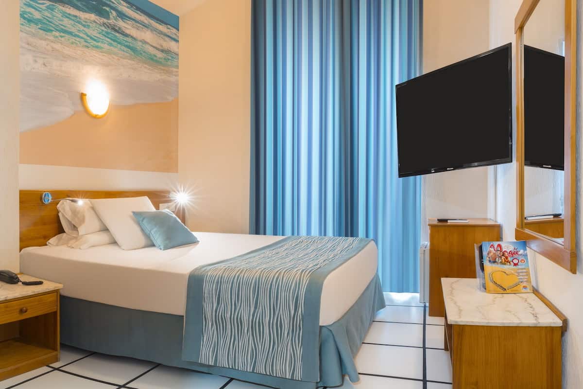 Habitación de hotel con cama, escritorio, silla, televisor y ventana con cortinas.