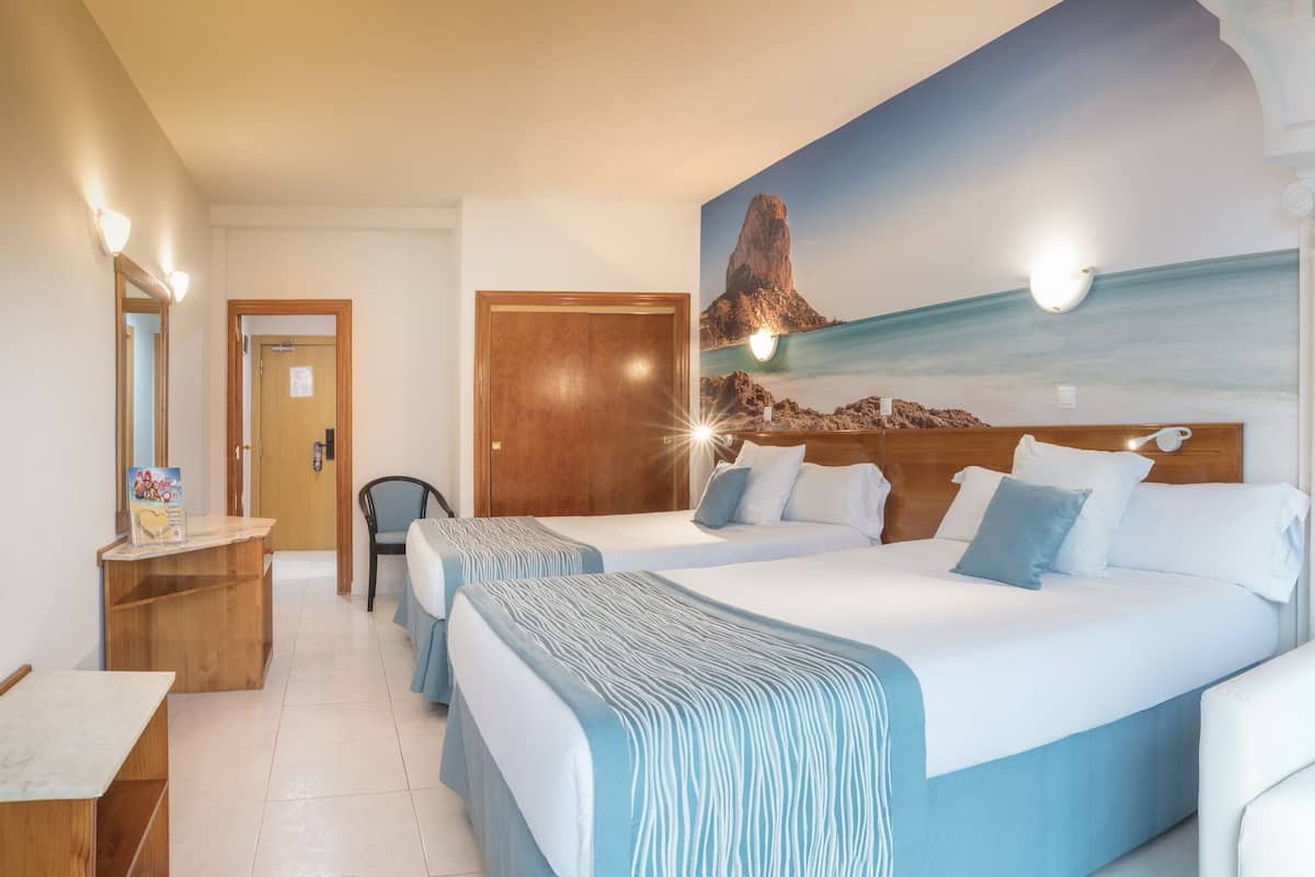 Habitación de hotel con dos camas, un escritorio de madera, una silla y un cuadro de un paisaje costero.