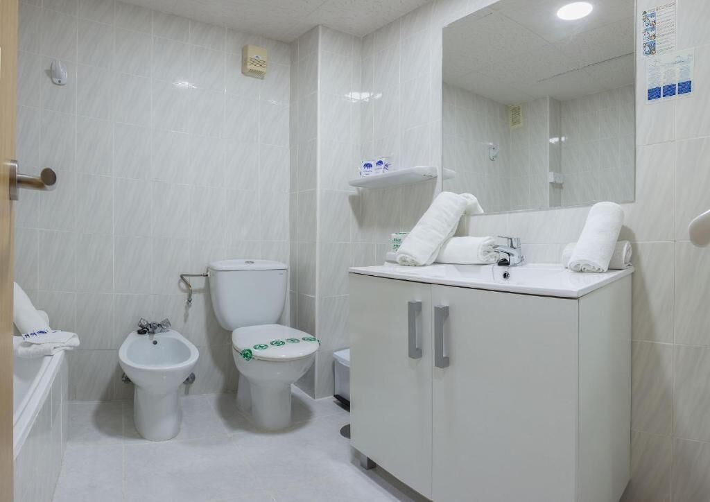 Un baño moderno con inodoro, bidé y bañera. Hay toallas sobre el lavamanos y un espejo encima.
