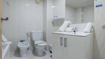 Un baño moderno con inodoro, bidé y bañera. Hay toallas sobre el lavamanos y un espejo encima.