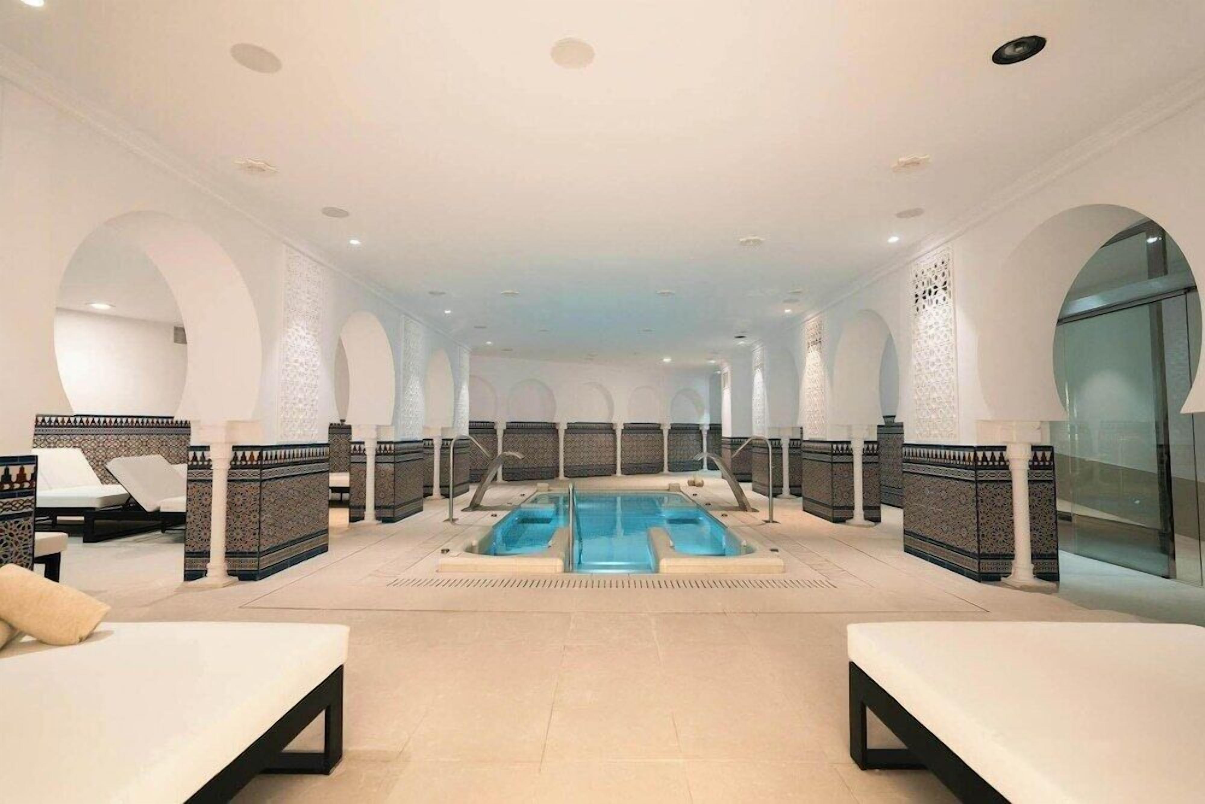 Un espace spa doté d’une piscine centrale, de coins salon et de murs aux motifs décoratifs.