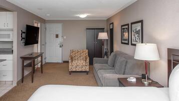Una habitación de hotel con cama, sofá, sillón, escritorio, televisión, lámpara y obras de arte en la pared.