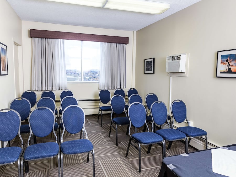 Une salle de conférence avec des rangées de chaises bleues, une grande fenêtre avec des rideaux et des tableaux encadrés accrochés aux murs.