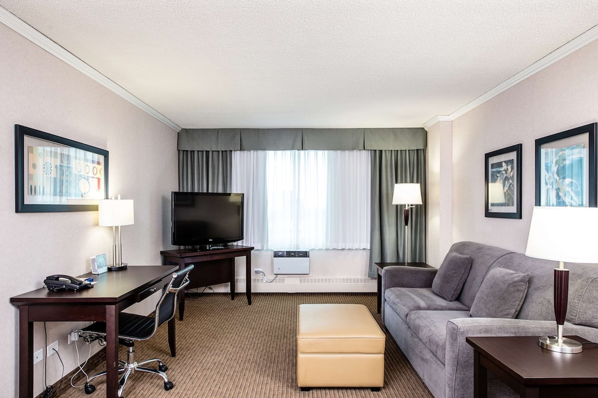 A hotel room with a desk, chair, television, sofa, and ottoman.