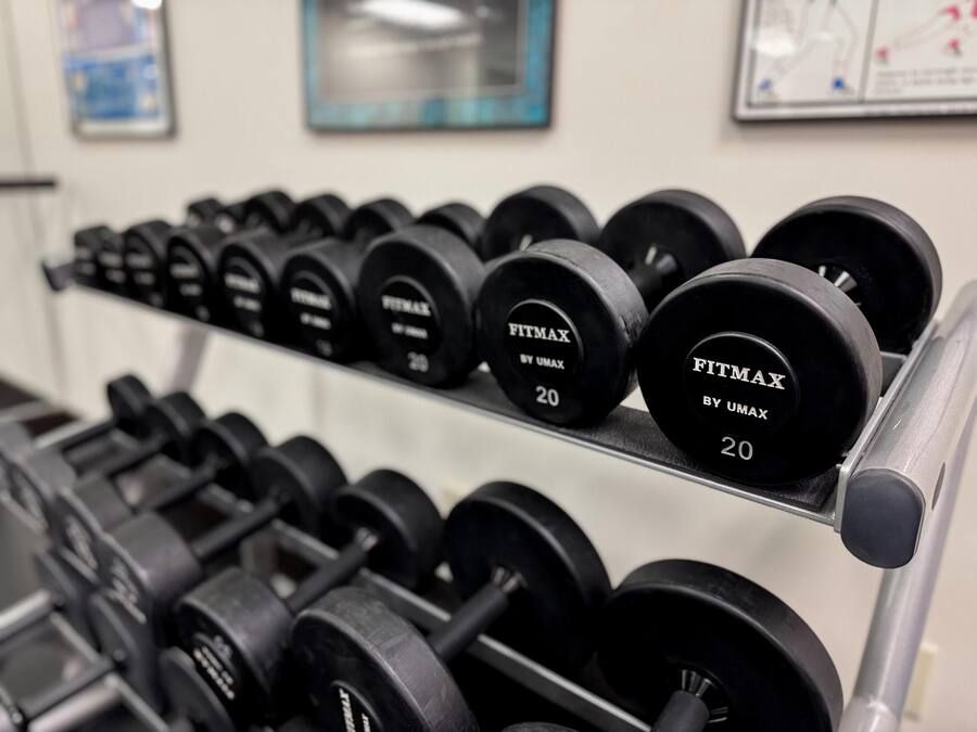 Um suporte com halteres pretos, identificados como 'FITMAX BY UMAX', com pesos marcados '20'.