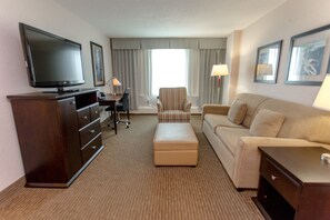 A hotel room with a flat-screen TV, a desk with a chair, a sofa, and an ottoman. - Campus Tower Suite Hotel (Edmonton)