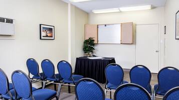A conference room with blue chairs, a black table, a whiteboard, and a plant.