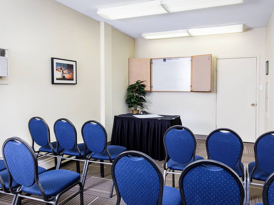 A conference room with blue chairs, a black table, a whiteboard, and a plant.