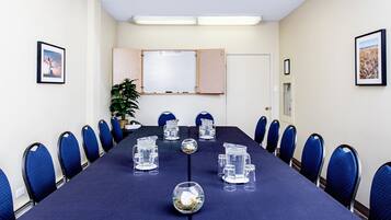 Een vergaderzaal met een lange tafel, blauwe stoelen en een whiteboard.