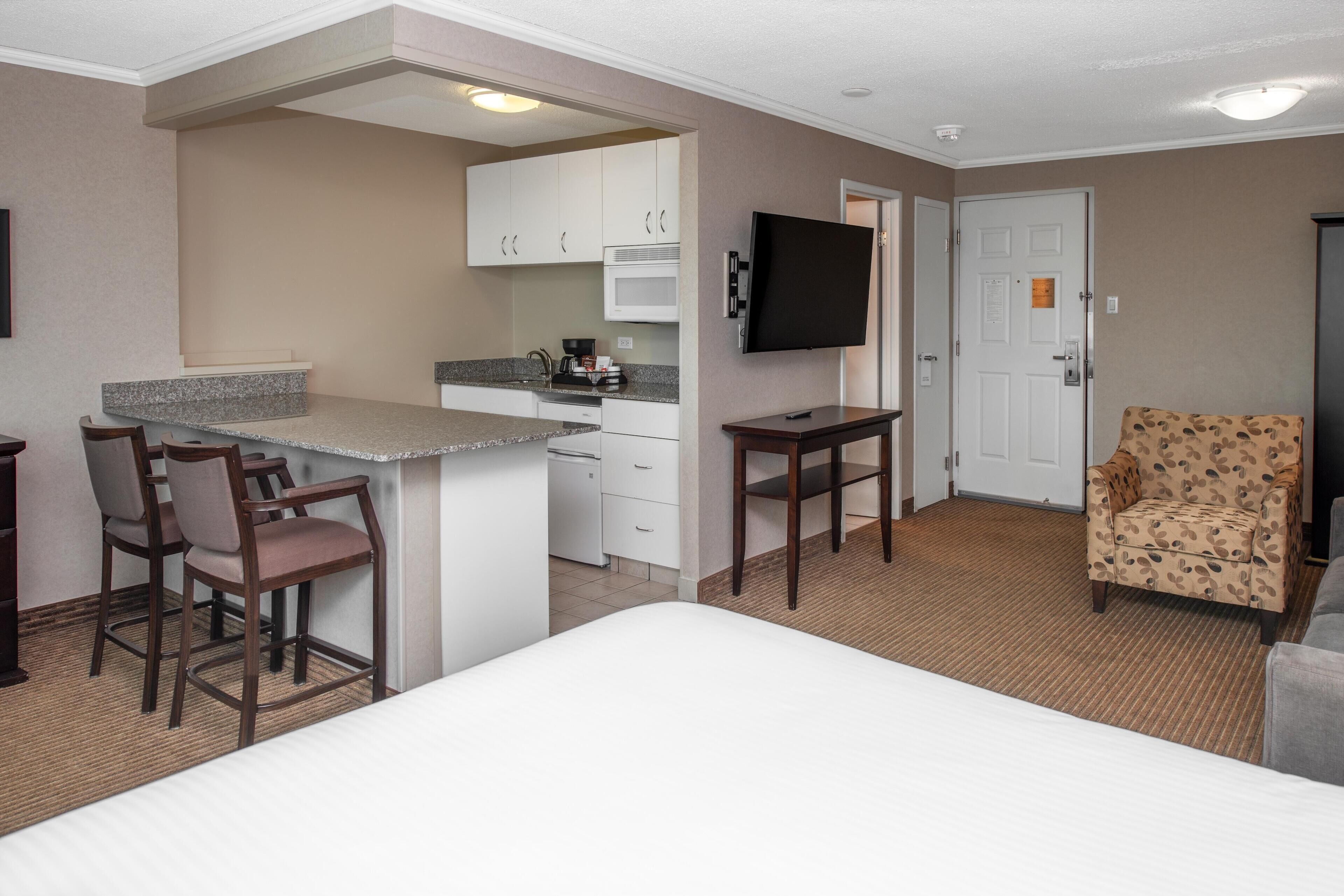 A hotel room with a bed, a kitchenette, a TV, and a patterned armchair.
