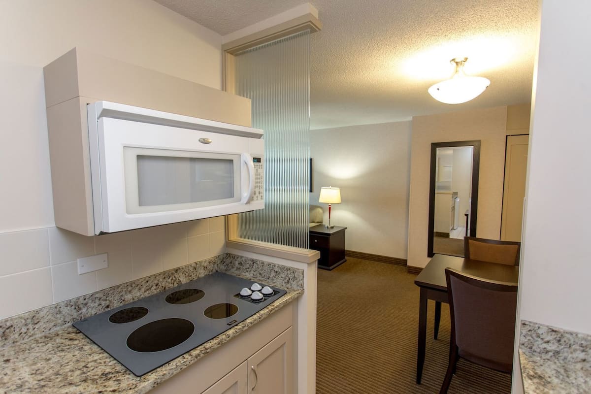A compact kitchenette with a microwave, stovetop, and a small table with a chair.