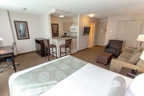 A hotel room with a bed, a desk, a chair, a sofa, and a kitchenette. - Campus Tower Suite Hotel (Edmonton)