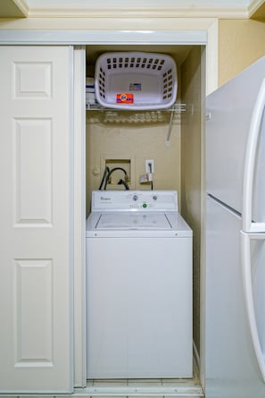 A compact laundry room with a Whirlpool washer and dryer, a Tide detergent box, and a white laundry basket on the wall. - Ventura at Boca Raton (Boca Raton)