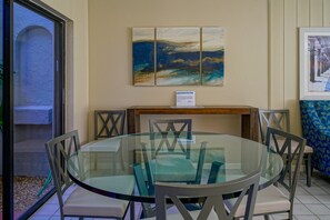A round glass table with chairs, a wooden sideboard, and artwork on the wall. - Ventura at Boca Raton (Boca Raton)