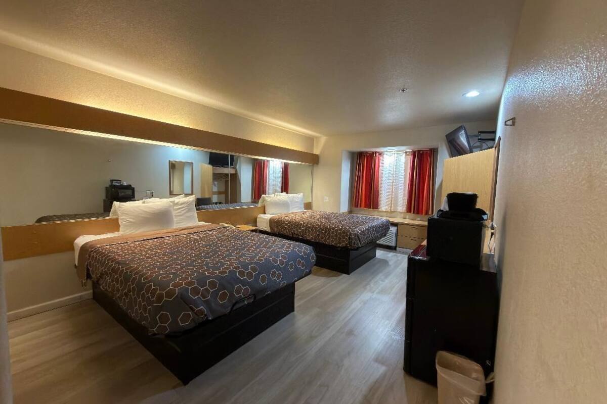 A hotel room with two beds, a desk, a chair, a mirror, and a window with curtains.