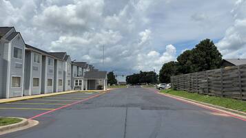 A parking lot with a row of motel-style buildings on one side and a wooden fence on the other.