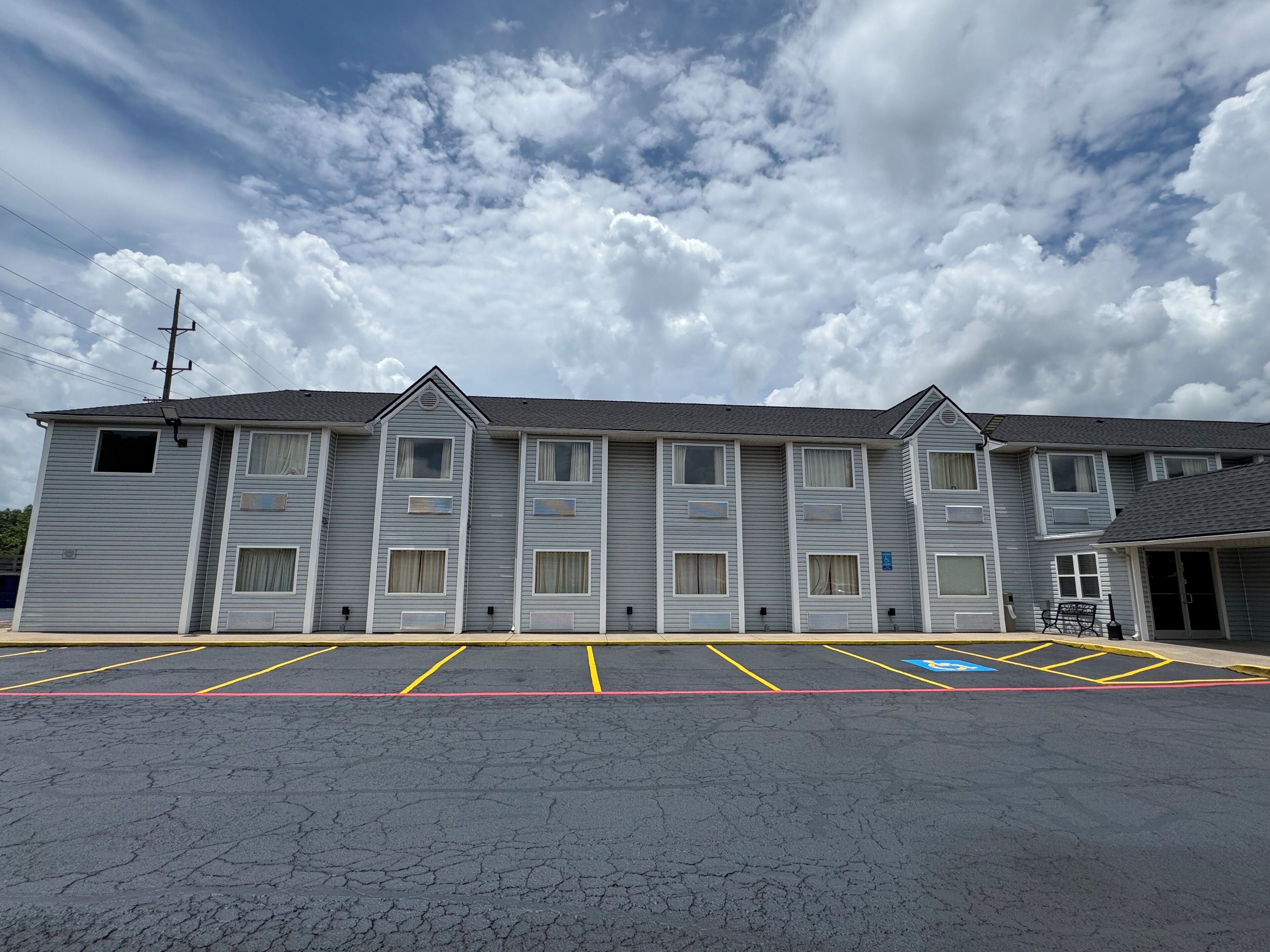 A motel with a row of rooms, a parking lot, and a clear sky.