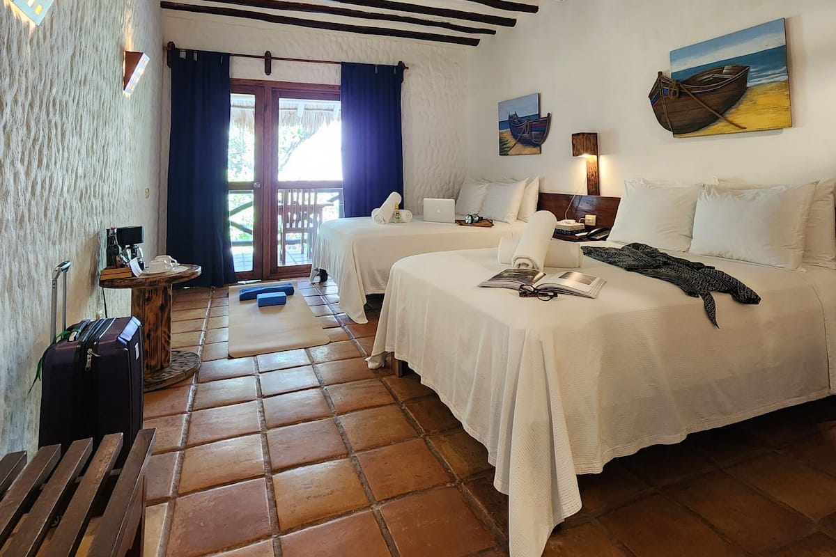 A room with two beds, a ceiling fan, a painting, and a view of the outdoors.