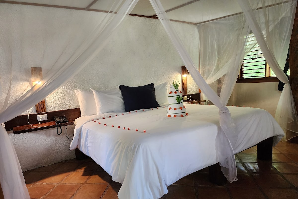 A bed with a canopy, white bedding, and a bedside table with a phone.