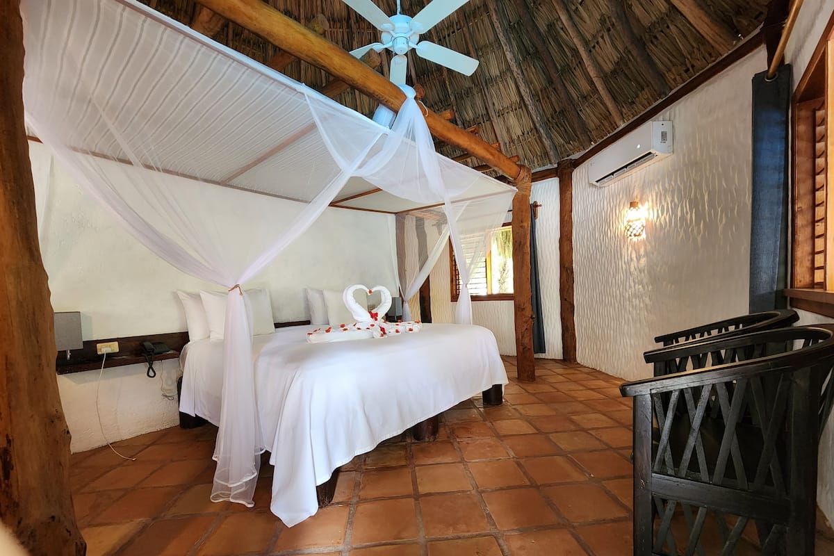 A room with a bed under a canopy, a wooden ceiling, and a tiled floor.