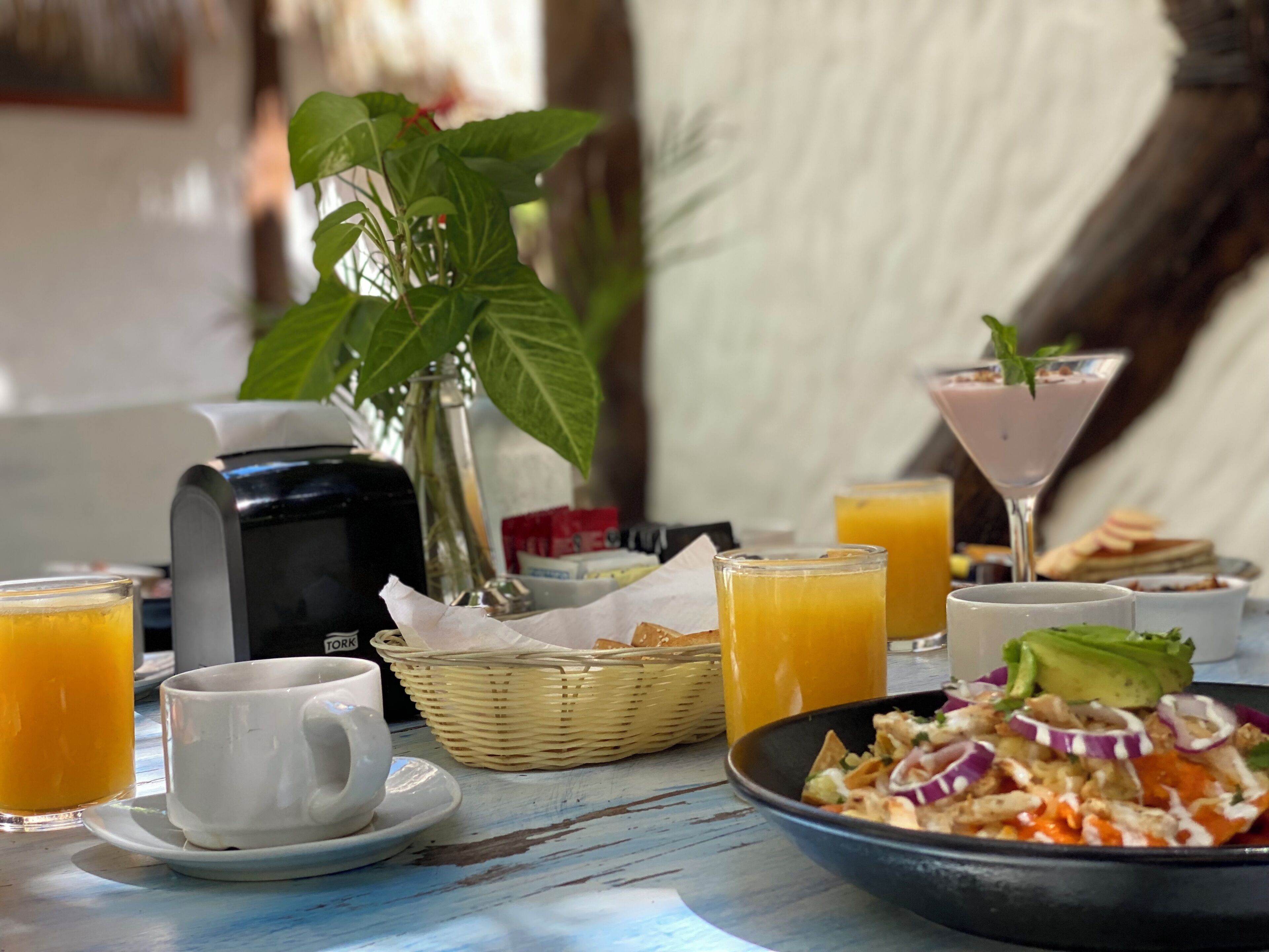 A breakfast table with orange juice, a white mug, a bowl of salad, and a martini glass.