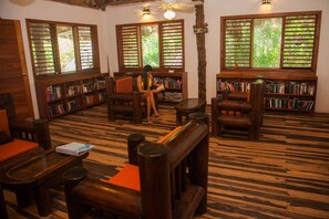 A library with wooden furniture, bookshelves, and large windows with blinds.
