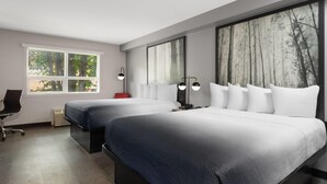 A modern hotel room with two beds, a desk, and a large window with a forest view.