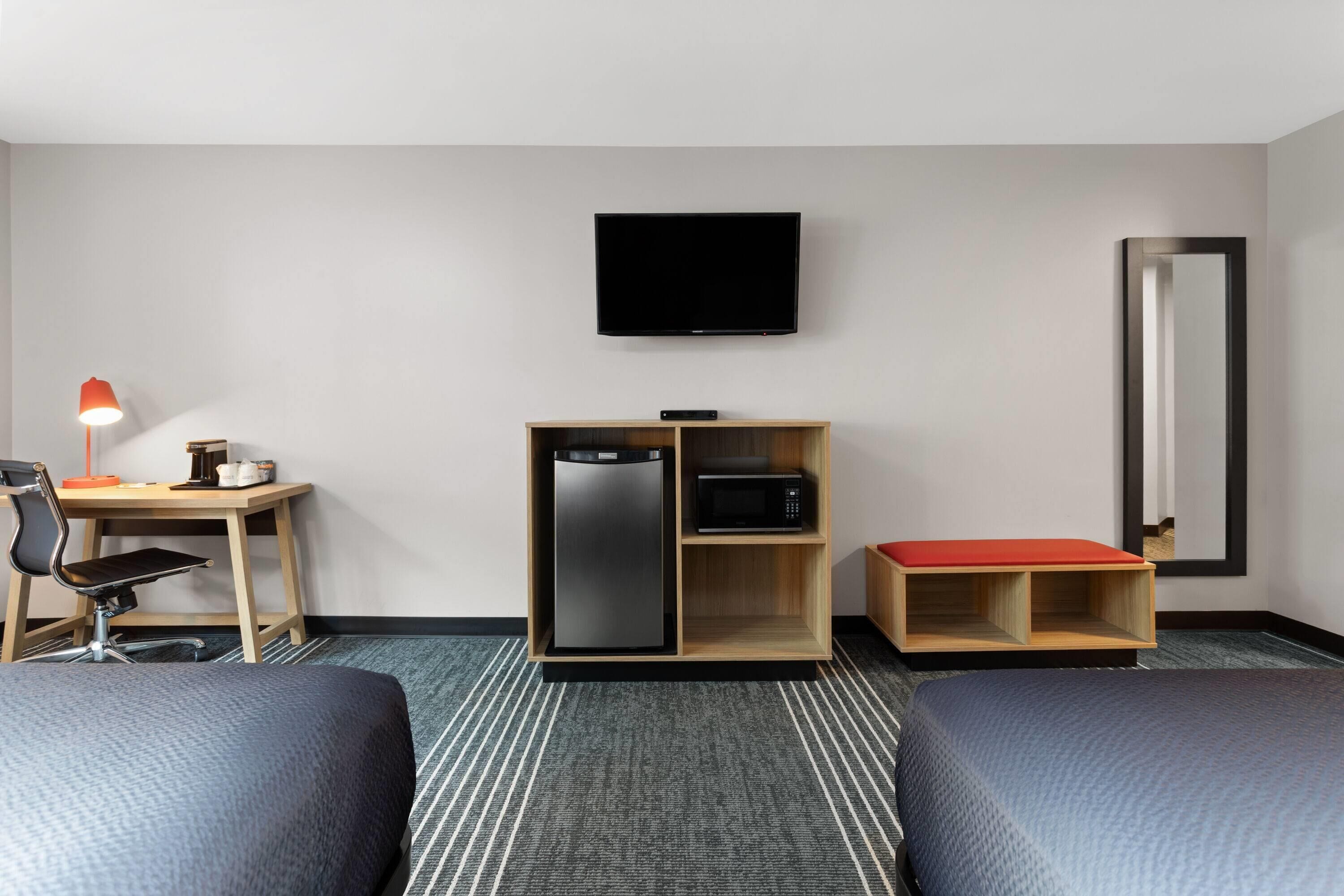 Een hotelkamer met twee bedden, een bureau met stoel, een televisie, een koelkast, een magnetron en een spiegel.