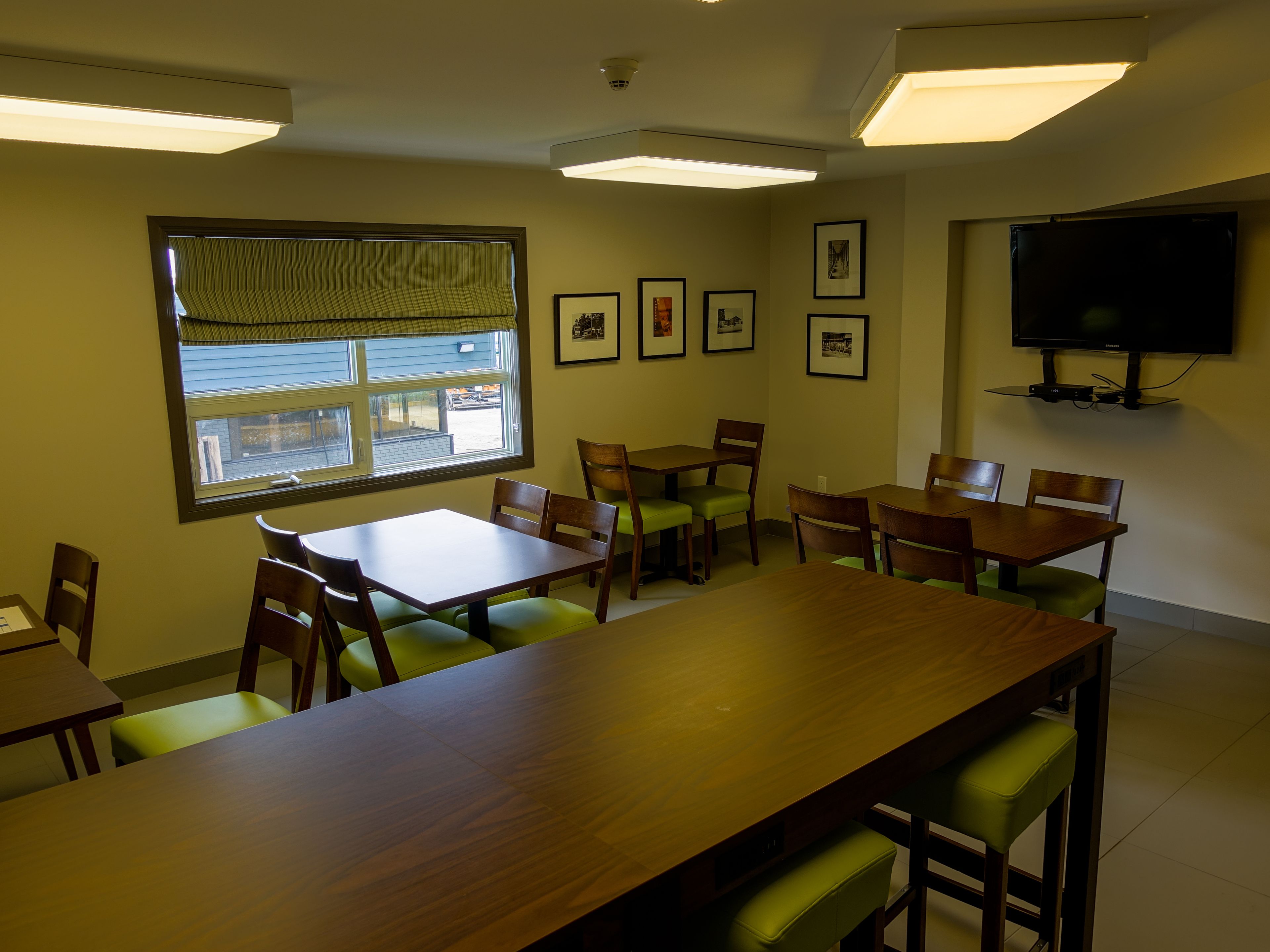 A conference room with a large table, several chairs, framed pictures on the wall, and a television mounted on the wall.