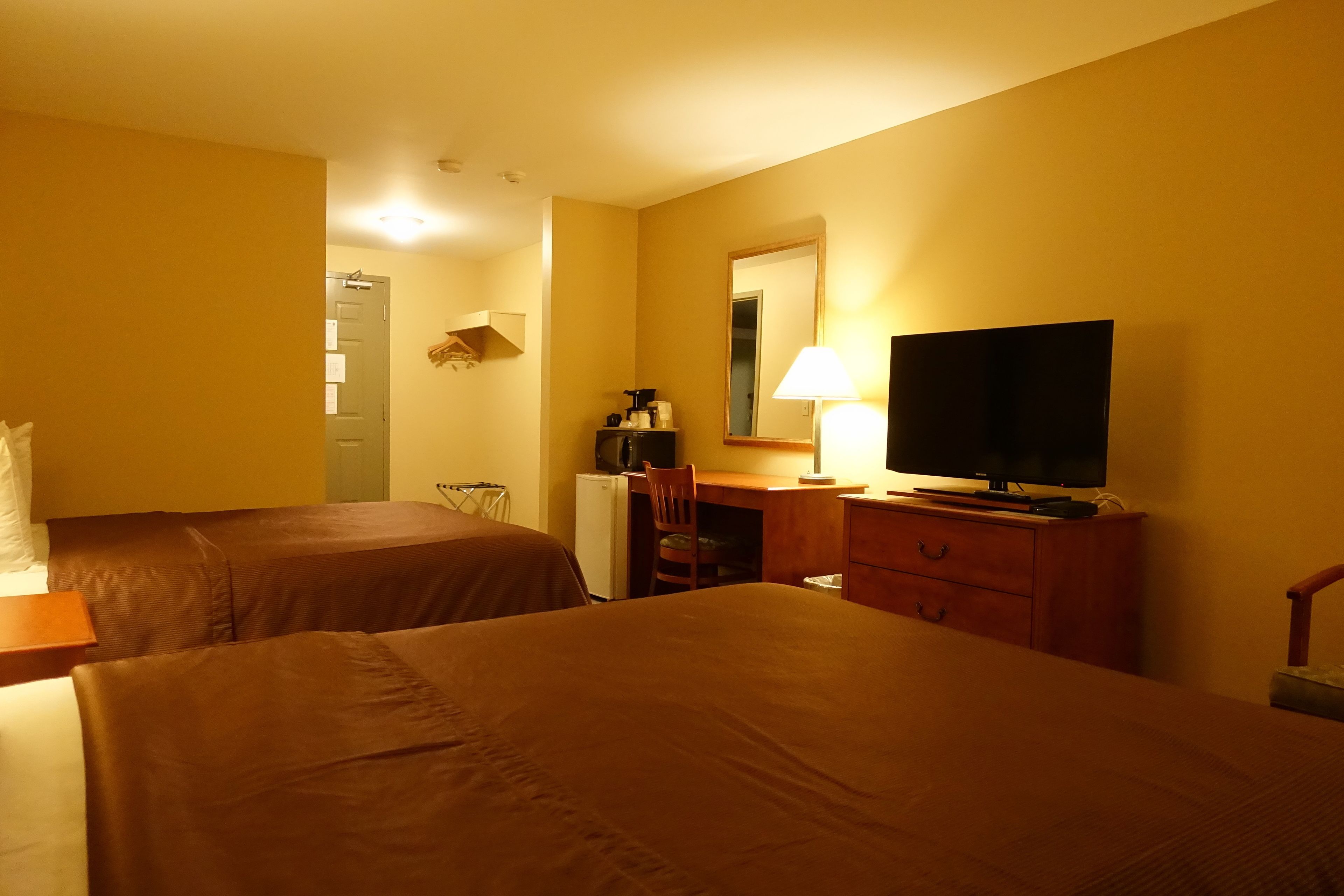 Een hotelkamer met twee bedden, een bureau met een lamp, een televisie en een kleine koelkast.