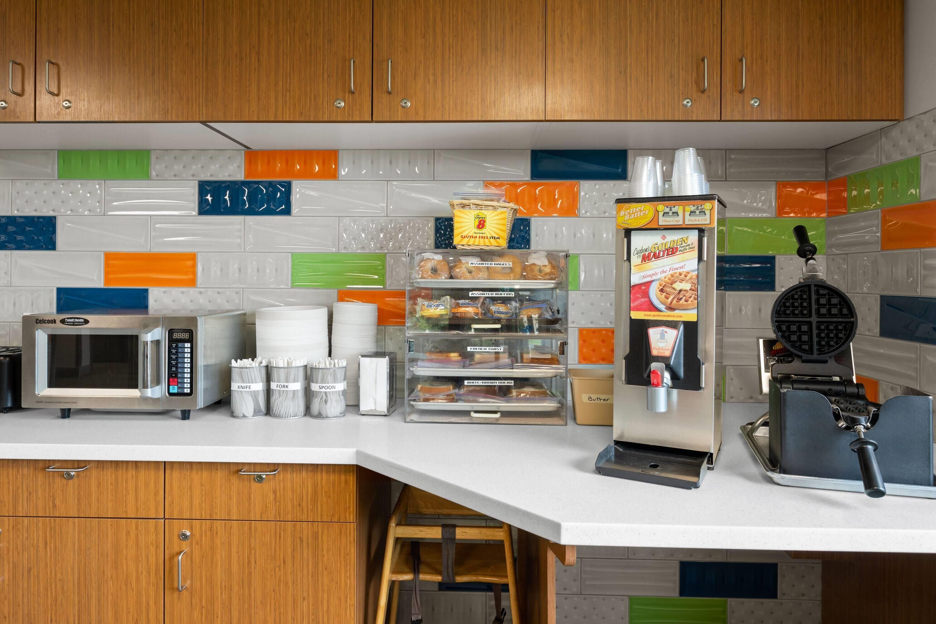 A kitchen with a microwave, toaster, waffle maker, and various food containers.