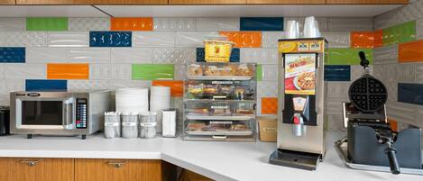 A kitchen with a microwave, toaster, waffle maker, and various food containers.