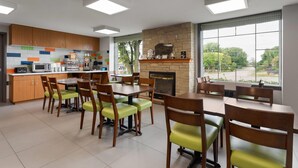 A modern kitchen with wooden cabinets, a stone fireplace, and large windows offering a view of the outdoors.