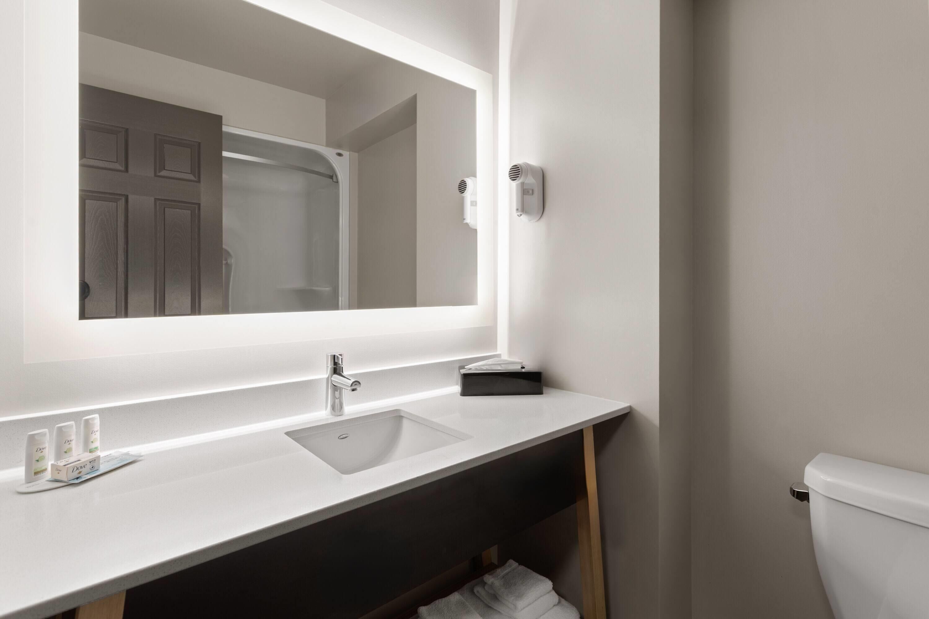 A modern bathroom with a large mirror, a white sink, and a toilet.
