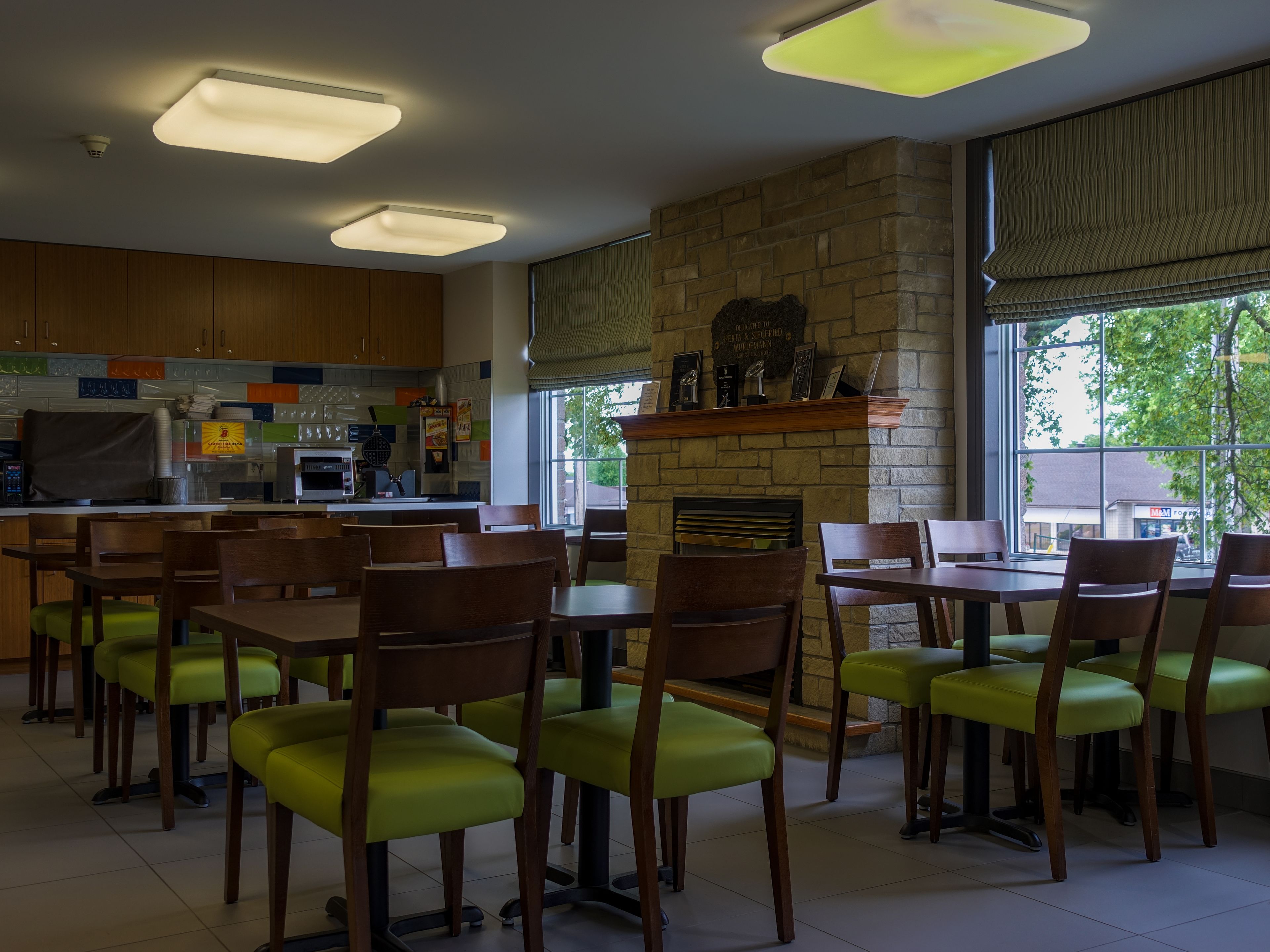 A restaurant with a stone fireplace, wooden tables and chairs, and a kitchen area with modern appliances.