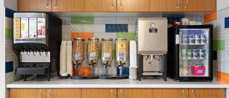 A kitchen area with a water dispenser, coffee machine, cereal dispensers, a refrigerator, and a mini-fridge.