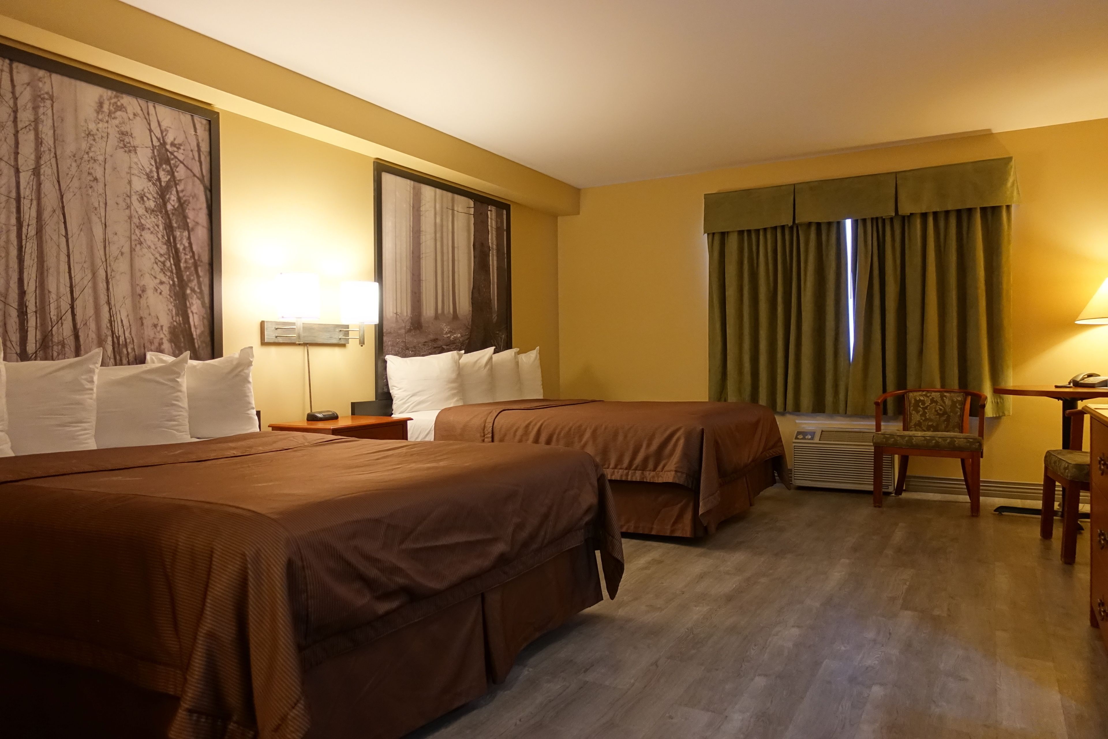 A hotel room with two beds, a desk, a chair, and a large window with curtains.