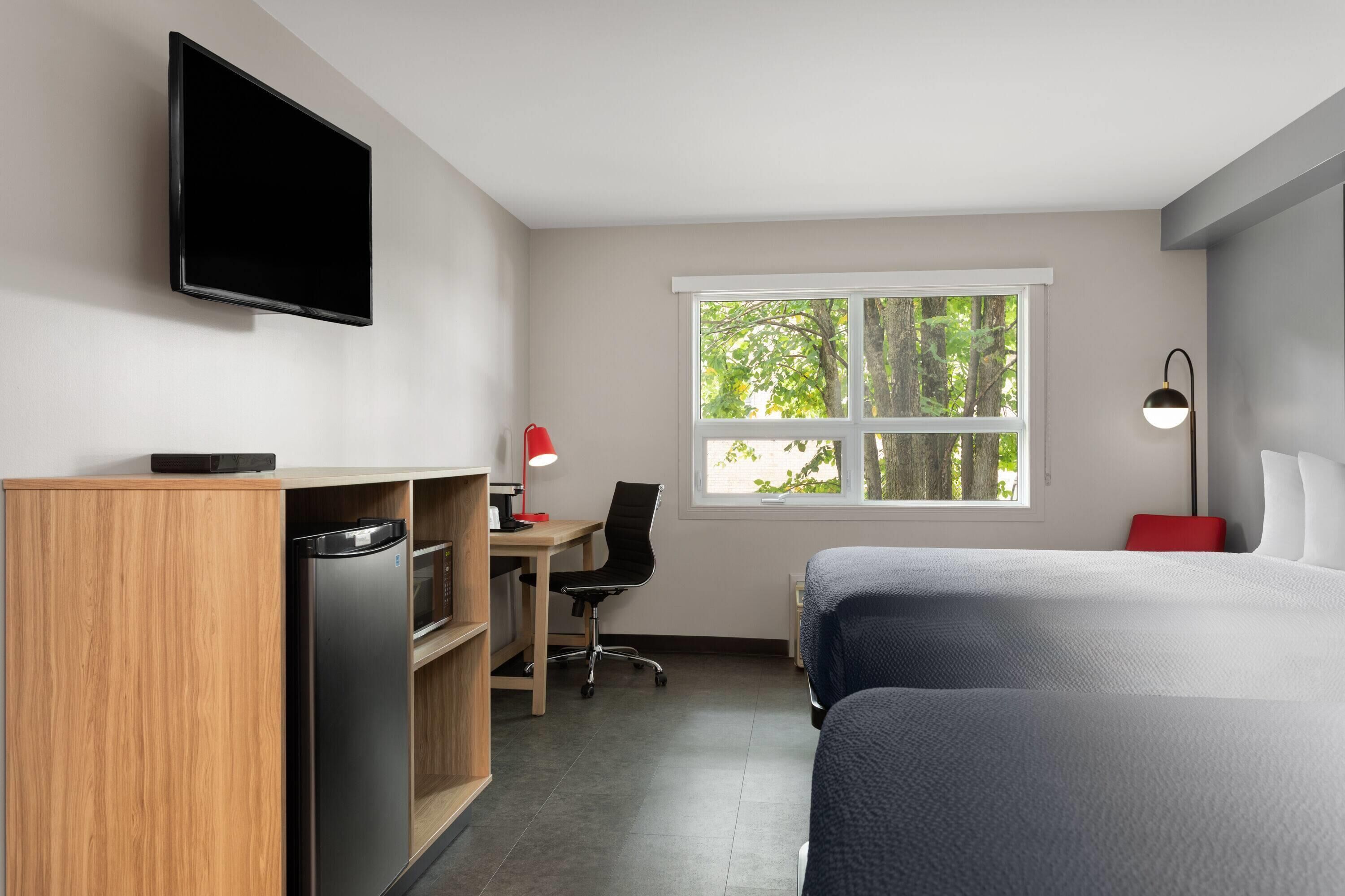 A hotel room with a bed, desk, chair, and a television on the wall.