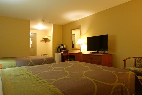 Habitación de hotel con dos camas individuales, un escritorio con lámpara, televisión y una pequeña cocina.